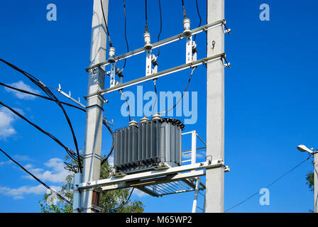 Eine elektrische Verteilung Transformator mit Kühlrippen auf der Pole. Gegen den blauen Himmel. Stockfoto