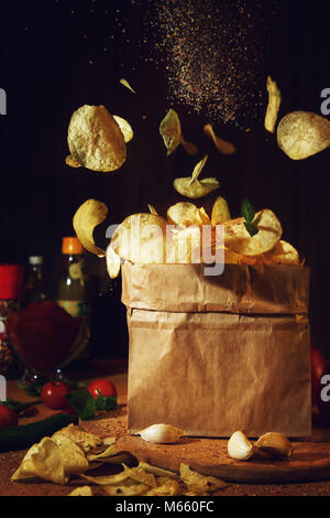 Flying Chips auf einem dunklen Hintergrund. Das Bild kann in der Werbung Verpackungen aus Papier oder einen Artikel über ungesunde Lebensmittel verwendet werden. Stockfoto