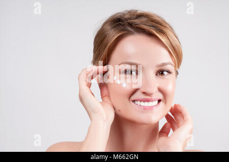 Schönheit und Hautpflege Konzept. Junge Frau mit Feuchtigkeitscreme auf. Schöne Mädchen, die kosmetische Creme auf die Haut in der Nähe der Augen. Stockfoto