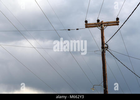 Alte hölzerne elektrische Säule mit Anschlüssen und Stromleitungen in alle Richtungen gegen stürmischen Himmel Stockfoto