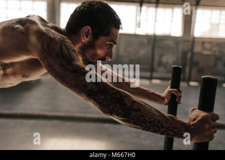 Starker junger Mann Drücken der Schlitten im Fitnessstudio. Muskulöse männlichen Athleten, intensiven körperlichen Training im Fitnessraum. Stockfoto