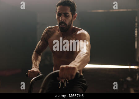 Fitness-Mann auf dem Fahrrad, der im Fitnessstudio dreht. Muskulöser junger Mann, der auf einem Fitnessrad trainiert. Stockfoto