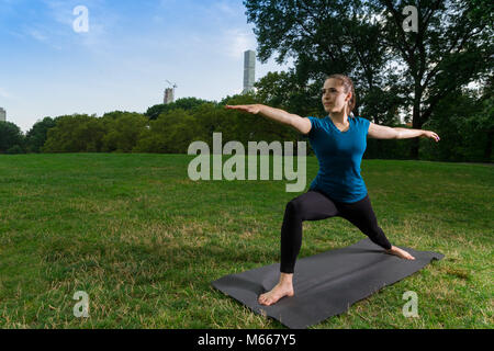 Junge kaukasier Frau übt Yoga im Central Park in New York City während trägt ein blaues Top, schwarze Leggings und barfuss Stockfoto