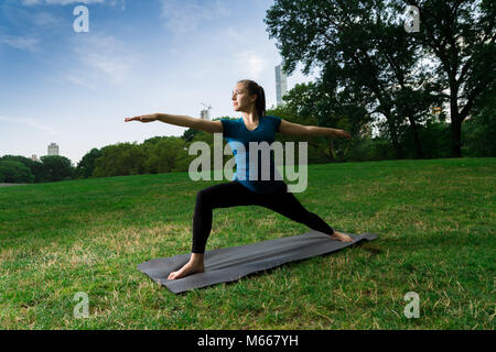 Junge kaukasier Frau übt Yoga im Central Park in New York City während trägt ein blaues Top, schwarze Leggings und barfuss Stockfoto