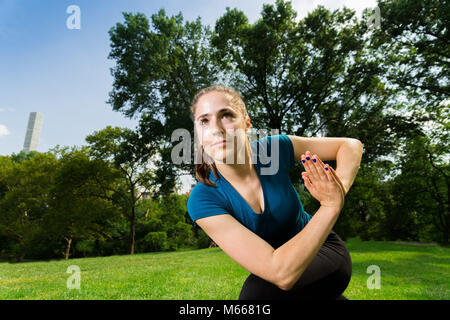 Junge kaukasier Frau übt Yoga im Central Park in New York City während trägt ein blaues Top, schwarze Leggings und barfuss Stockfoto