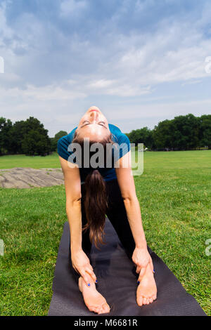 Junge kaukasier Frau übt Yoga im Central Park in New York City während trägt ein blaues Top, schwarze Leggings und barfuss Stockfoto