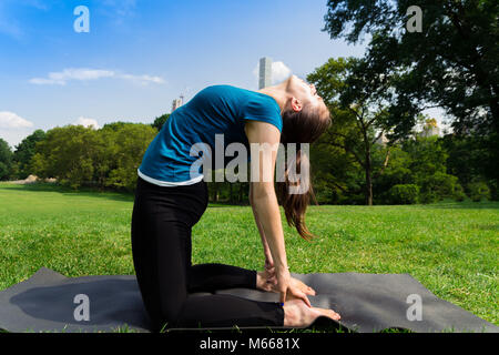 Junge kaukasier Frau übt Yoga im Central Park in New York City während trägt ein blaues Top, schwarze Leggings und barfuss Stockfoto
