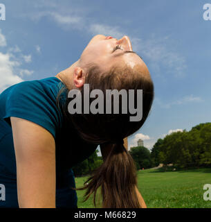 Junge kaukasier Frau übt Yoga im Central Park in New York City während trägt ein blaues Top, schwarze Leggings und barfuss Stockfoto