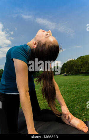Junge kaukasier Frau übt Yoga im Central Park in New York City während trägt ein blaues Top, schwarze Leggings und barfuss Stockfoto