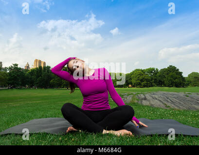 Junge kaukasier Frau übt Yoga im Central Park in New York City beim Tragen eines Magenta Top, schwarze Leggings und barfuss Stockfoto