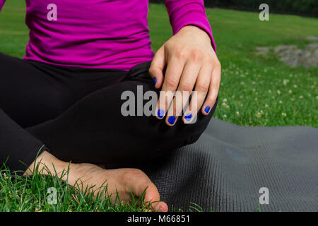 Junge kaukasier Frau übt Yoga im Central Park in New York City beim Tragen eines Magenta Top, schwarze Leggings und barfuss Stockfoto