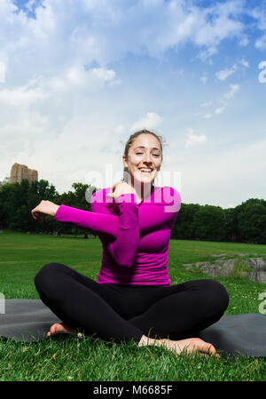Junge kaukasier Frau übt Yoga im Central Park in New York City beim Tragen eines Magenta Top, schwarze Leggings und barfuss Stockfoto