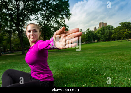 Junge kaukasier Frau übt Yoga im Central Park in New York City beim Tragen eines Magenta Top, schwarze Leggings und barfuss Stockfoto