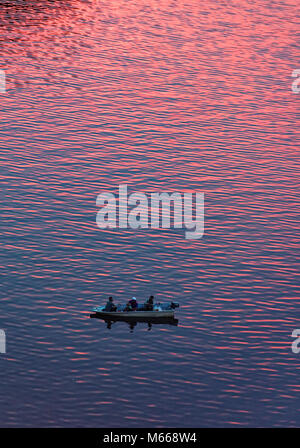 Drei Männer Fischen am Sarawak River in Kuching wie der Sonnenuntergang macht das Wasser rot Stockfoto