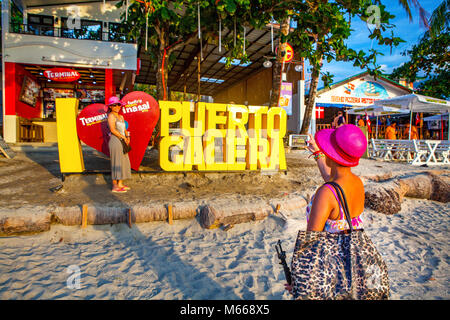 Weibliche Filipino Touristen in hot pink Hüte nehmen selfies vor der ich Puerto Galera sign am weißen Strand Liebe, Oriental Mindoro, Philippinen. Stockfoto