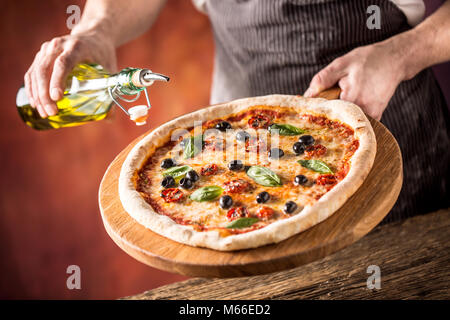 Koch und Pizza. Koch gießen Olivenöl auf Pizza im Hotel oder im Restaurant. Stockfoto