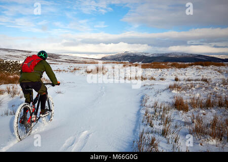Skipton, North Yorkshire, UK - 27. Februar 2018: eine Person fährt Mountainbike off road durch Schnee an einem sonnigen Tag in der North Yorkshire Dales Stockfoto