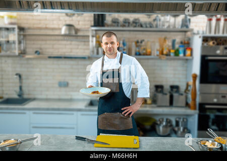 Gerne männliche Küchenchef präsentiert die Schüssel in der gewerblichen Küche Innenraum Stockfoto