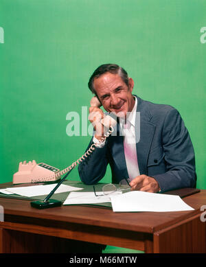 1970er lächelnd REIFER MANN MIT ANZUG HOLDING BRILLE sitzt am Schreibtisch im TELEFON MIT KAMERA-ko 626 HAR 001 HARS STIL KOMMUNIKATION KAUKASISCHEN GERNE FREUDE LIFESTYLE ELDER STUDIO SHOT GROWNUP EINE PERSON NUR KOMMUNIKATION KOPIEREN RAUM MIT HALBER LÄNGE GROWN-UP IM INNENBEREICH Nostalgie im mittleren Alter Mann im mittleren Alter ARBEITSPLATZ AUGENKONTAKT 40-45 Jahre 45-50 JAHRE WHITE COLLAR VERKAUF GLÜCK FRÖHLICHE BESCHÄFTIGUNG KRAWATTE TELEFONE LÄCHELT FRÖHLICH ELEKTRISCHES GERÄT TELEFONE KOMMUNIZIEREN VERKÄUFER MITARBEITER PANORAMABLICK MÄNNER KAUKASISCHEN ETHNIE AUF KAMERA BERUFE ALTMODISCHE PERSONEN Stockfoto