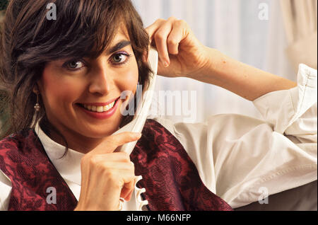 1990 s JUNGE FRAU AM TELEFON IN DIE KAMERA LÄCHELN - Ks 35045 DEG 002 HARS NOSTALGIE AUGENKONTAKT 20-25 JAHRE BRUNETTE einzelnes Objekt GLÜCK KOPF UND SCHULTERN HEITER 18-19 JAHRE 1990 s PHONES LÄCHELT VERBINDUNG FREUDIGE TELEFONE JUNGEN ERWACHSENEN FRAU LÄSSIG KAUKASISCHEN ETHNIE AUF KAMERA ALTMODISCHE PERSONEN Stockfoto