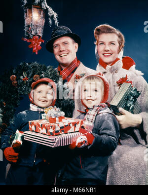 1950 s Familie Mann Frau zwei Kinder, WEIHNACHTSGESCHENKE LÄCHELND steht unter der Laterne - KX2215 HAR 001 HARS SUBURBAN URBAN XMAS FARBE MÜTTER ALTE ZEIT ÜBERRASCHUNG BRUDER OLD FASHION SCHWESTER JUGENDLICHER STIL WILLKOMMEN FRIEDEN LATERNE KAUKASISCHEN SÖHNE FREUEN FREUDE LIFESTYLE RELIGION FEIER FRAUEN VERHEIRATETE BRÜDER EHEPARTNER EHEMÄNNER HOME LEBEN FREUNDSCHAFT IN VOLLER LÄNGE TÖCHTER INSPIRATION INTERESSIEREN GESCHWISTER SPIRITUALITÄT VERTRAUEN SCHWESTERN NOSTALGIE VÄTER MITEINANDER 25-30 JAHRE 3-4 JAHRE 30-35 JAHRE 5-6 JAHRE FREIHEIT ERFOLG FRAUEN GLÜCK FRÖHLICHE MÜTTER VÄTER AUFREGUNG LEISTUNGSSTARKE ERHOLUNG GESCHWISTER Stockfoto