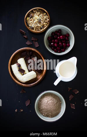 Muffins Zutaten: Milch, Müsli, gefroren Cherry, Flachs, Mehl, Banane und Schokolade auf schwarzem Hintergrund Stockfoto
