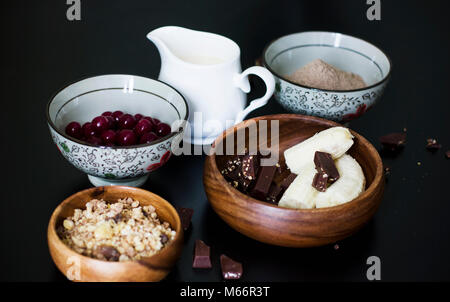 Muffins Zutaten: Milch, Müsli, gefroren Cherry, Flachs, Mehl, Banane und Schokolade auf schwarzem Hintergrund Stockfoto