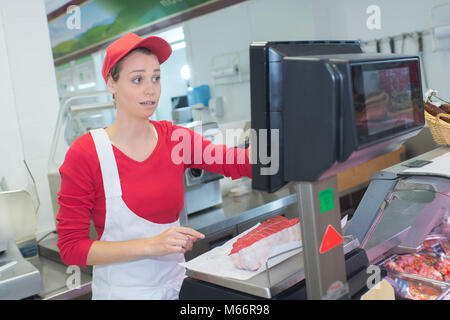 Gerne Mitte erwachsene Frau mit einem Gewicht von Fleisch auf der Skala bei Metzgerei Stockfoto