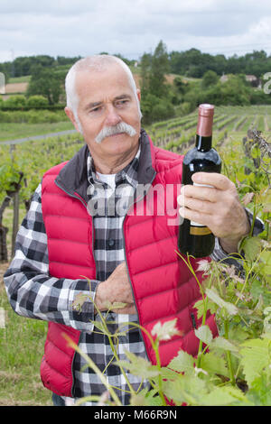 Winzer auf seinem Weinberg mit einer Flasche Wein Stockfoto