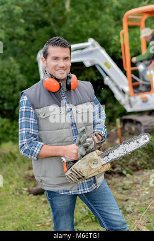 Mann mit Kettensäge, Digger im Hintergrund Stockfoto
