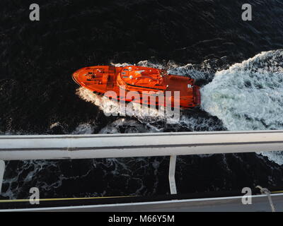 Farbenfrohe Sicherheit Boot führt die riesiges Kreuzfahrtschiff von dem Hafen in Stockholm, Schweden. Helles orange boat Beschleunigung in den weiten, blauen Ozean. Stockfoto