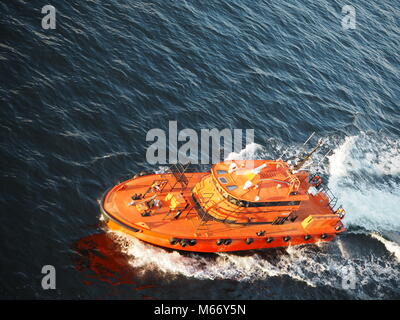 Farbenfrohe Sicherheit Boot führt die riesiges Kreuzfahrtschiff von dem Hafen in Stockholm, Schweden. Helles orange boat Beschleunigung in den weiten, blauen Ozean. Stockfoto