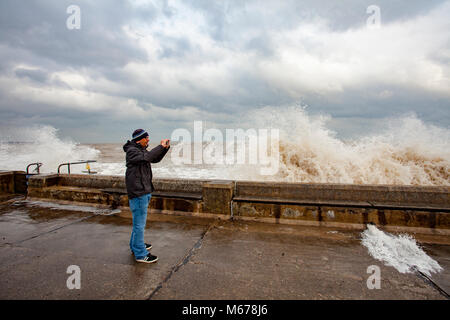 Ein Mann die Bilder der Brandung an der Promenade Wand in Colwyn Bay, Wales als Ergebnis des Tieres aus dem Osten und Sturm Emma riesige zerstörerische Wellen entlang der Küste Stockfoto
