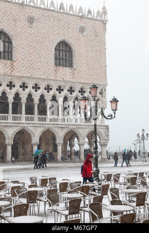 Venedig, Venetien, Italien, 1. März 2018. Schlechtes Wetter in Venedig heute mit Sub-Temperaturen zwischen minus 3 und minus 2 und kontinuierliche Schnee den ganzen Tag durch das Tier aus dem Osten, oder die Sibirische Front aus Russland quer durch Europa verursacht. Asiatische Tourist in Rot wandern zwischen Restaurant Tabellen in Piazza San Marco mit dem Dogenpalast hinter sich. Stockfoto