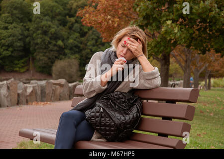 Frau hat die Erkältung oder Grippe. Husten. Mädchen sitzt auf der Bank im Park Stockfoto