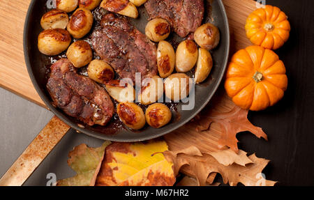 Roastbeef Steak mit gerösteten Kartoffeln in Kupfer Pfanne auf Holztisch, Ansicht von oben. Herbstliche Stimmung Stockfoto