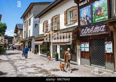Frankreich. Blick auf die Straße mit Shop, Kino und Frau mit Hund in Megeve. Ein bekannter Wintersportort in der Nähe des Mont Blanc in den Französischen Alpen. Stockfoto