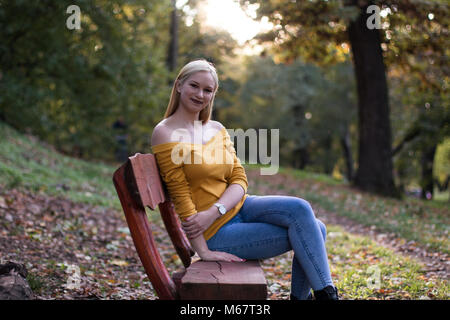 Junge hübsche blonde Frau sitzt auf einer Holzbank im Park, Natur genießen Stockfoto