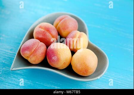 Pfirsiche reifen Frucht in Herzform Teller auf einem blauen vintage Holz- Hintergrund Stockfoto