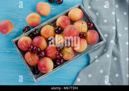 Pfirsiche und Kirschen reif frisches Obst im Korb auf einem hölzernen Hintergrund Stockfoto