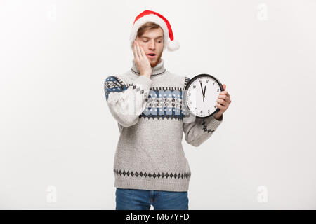 Urlaub Konzept - Junge glücklich aussehenden Bart Mann in Pullover Holding weisse Uhr über weiße studio Hintergrund. Stockfoto