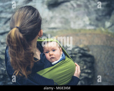 Eine junge Mutter ist draußen in der Natur mit ihrem Baby im Tragetuch Stockfoto