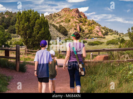 Junge Frau mit zwei Kindern wandern rund um Garten der Götter Park in Colorado Springs, Colorado; Felsformationen und blauer Himmel im Hintergrund Stockfoto