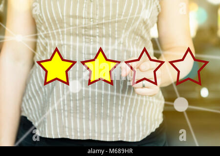 Frau zeigt mit dem Finger auf ein Rating Sterne Konzept an einem sonnigen Tag. Stockfoto