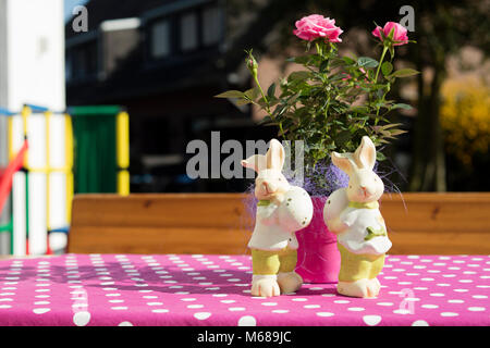 Ostern Kaninchen Figuren auf einem rosa Tabelle mit einer Rose in einem sonnigen Tag. Stockfoto