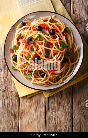 Spaghetti alla putanesca mit Sardellen, Tomaten, Knoblauch und schwarzen Oliven close-up auf einem Teller. Vertikal oben Ansicht von oben Stockfoto