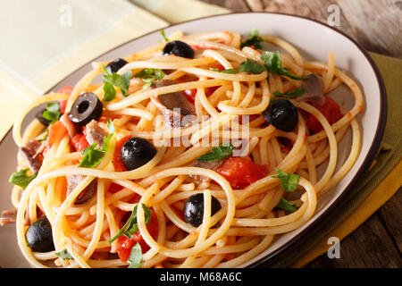 Italienisches Essen: Spaghetti alla putanesca mit Sardellen, Tomaten, Knoblauch, schwarzen Oliven und grünen Close-up auf einem Teller. Horizontale Stockfoto