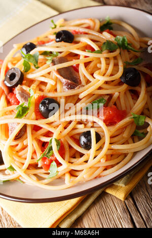 Italienische Pasta alla Puttanesca mit Sardellen, Tomaten, Knoblauch und schwarzen Oliven Makro auf einem Teller. Vertikale Stockfoto