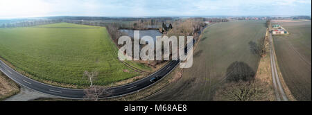 Composite Panorama von Luftaufnahmen und Luftaufnahmen von einer geraden Straße neben einem Teich und einem Feld, abstrakte Wirkung durch Verzerrung aufgrund der Stockfoto