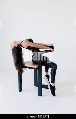 Seite in voller Länge ansehen Der flexiblen sportwoman in Sportbekleidung posiert auf dem Stuhl und dehnen ihr zurück auf weißen Hintergrund. Stockfoto